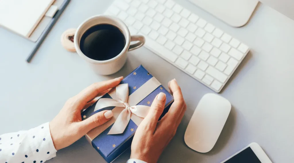 Professional workspace showing hands wrapping corporate gifts with coffee and keyboard, showcasing corporate gifting services UAE.