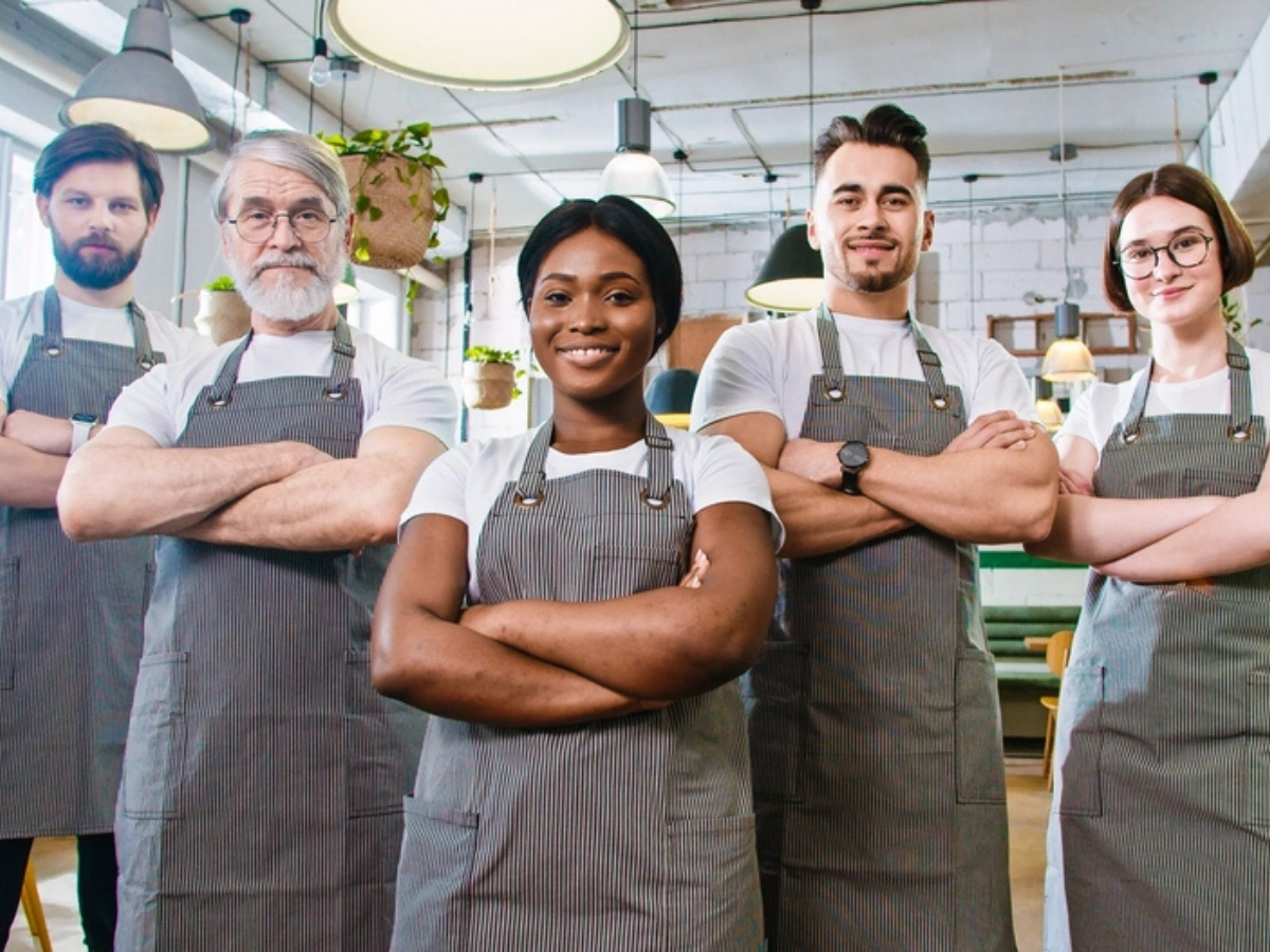 Diverse café team wearing café staff uniforms posing confidently under hanging lights, café staff uniforms UAE.