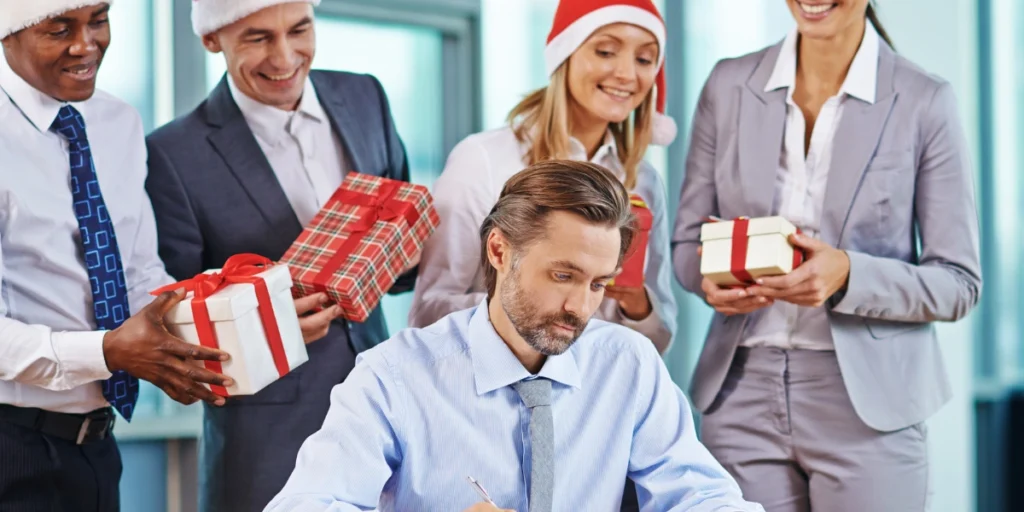 Office team in Santa hats surprising a colleague with wrapped presents, showcasing festive christmas corporate gifts uae.
