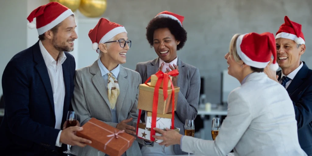 Coworkers in Santa hats exchanging wrapped presents and laughing during an office party, highlighting christmas corporate gifts uae.