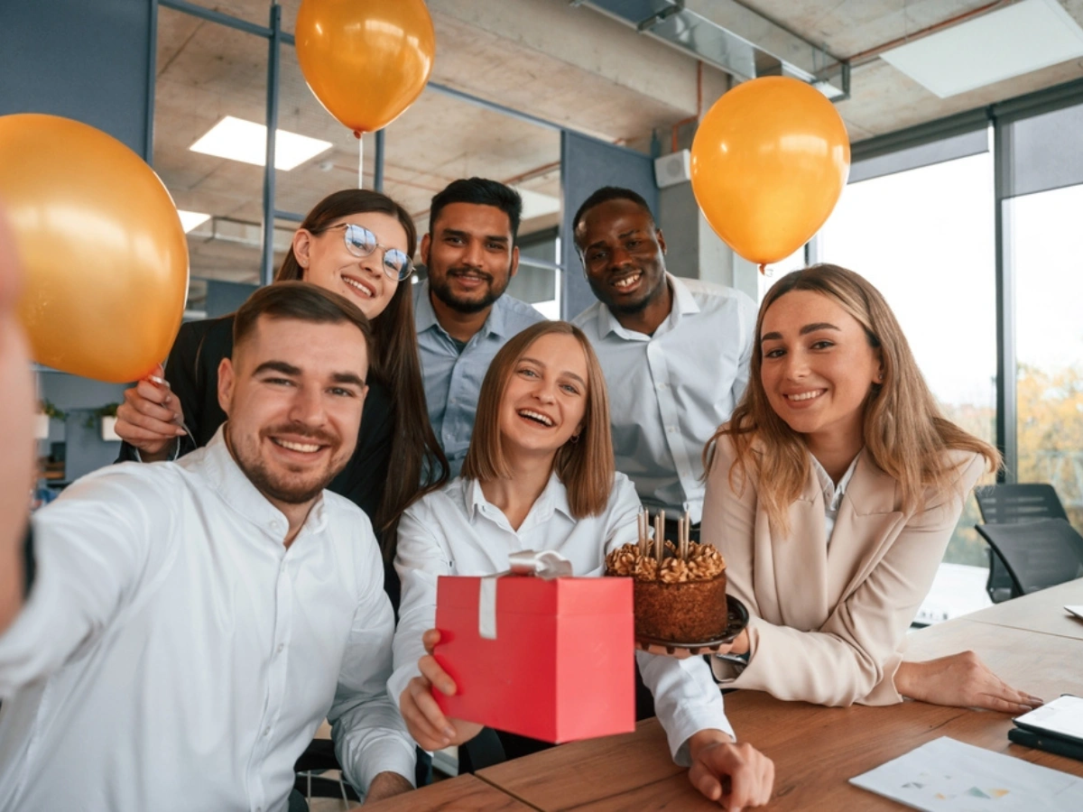 Diverse team celebrating with balloons and a gift box promoting Sustainable Corporate Gifts Dubai.